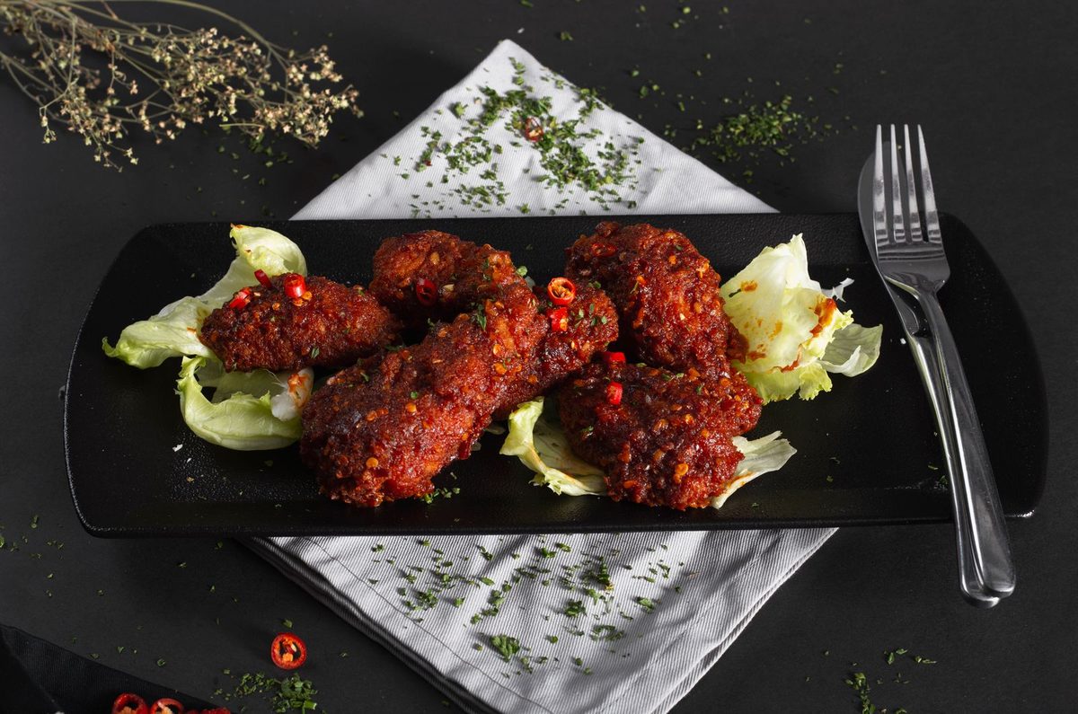 Spicy chicken wings on a black plate with lettuce and a fork