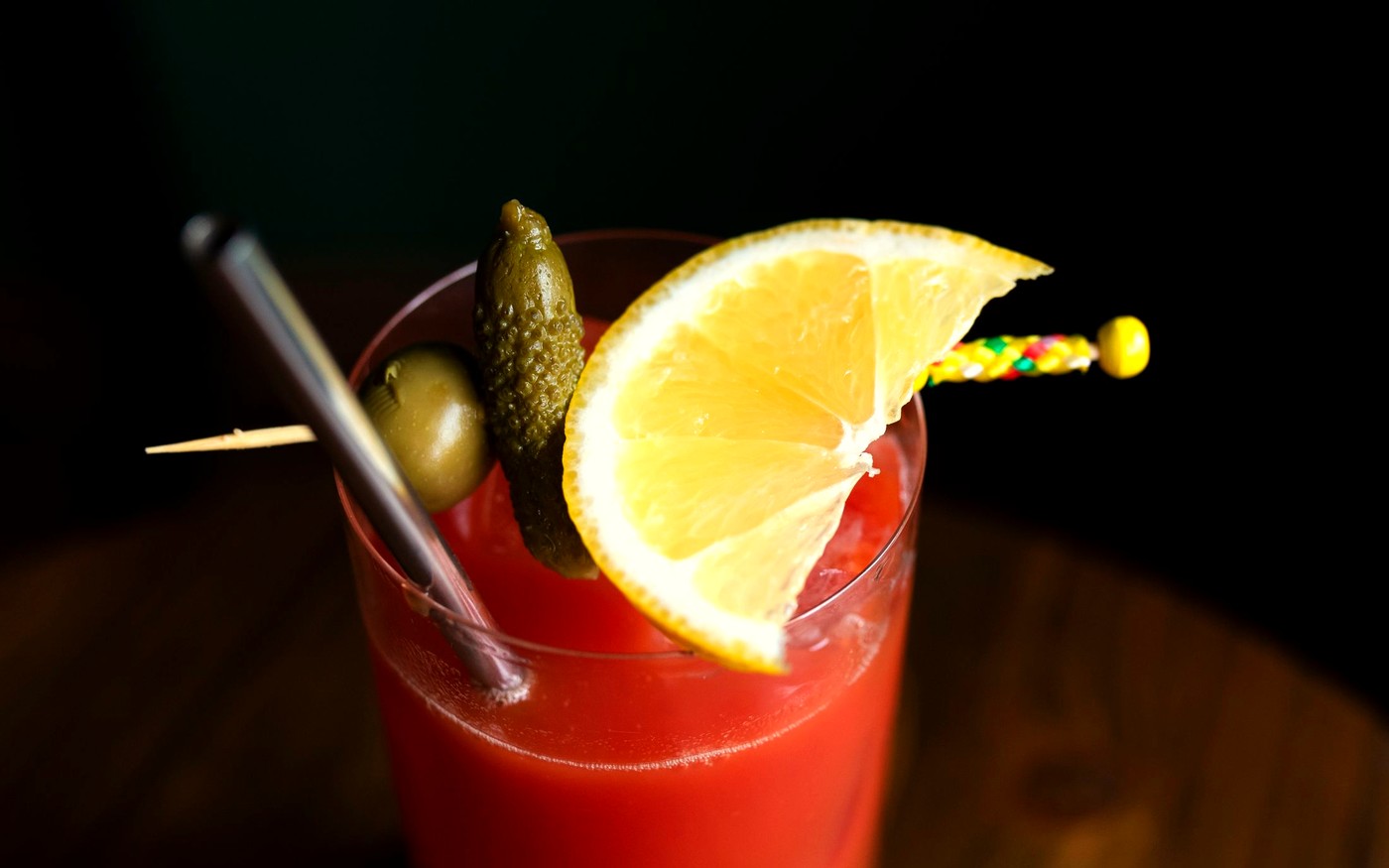 A Bloody Mary garnished with lemon and pickle on a dark bar
