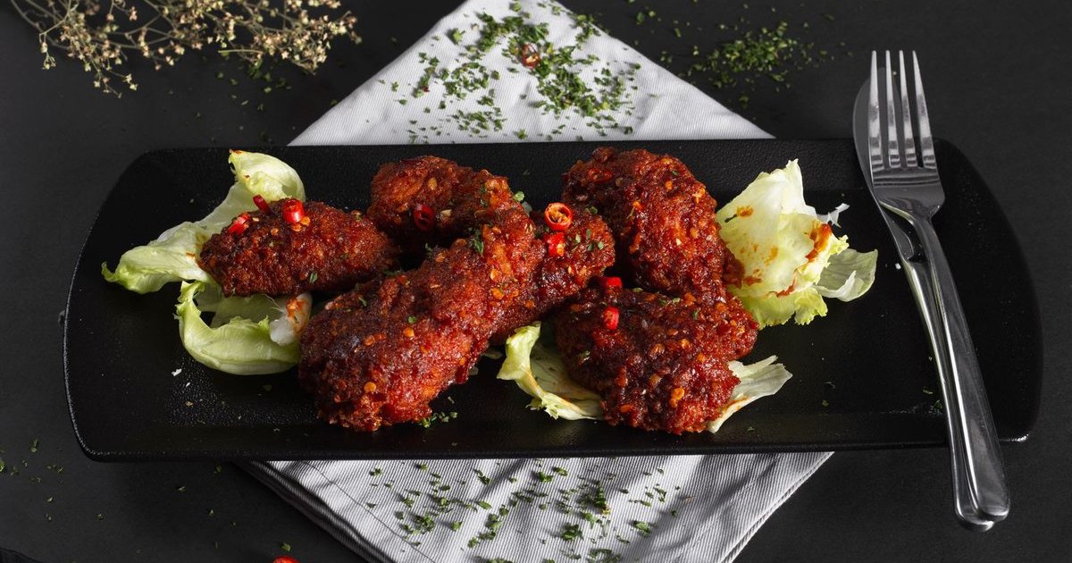 Spicy chicken wings on a black plate with lettuce and a fork
