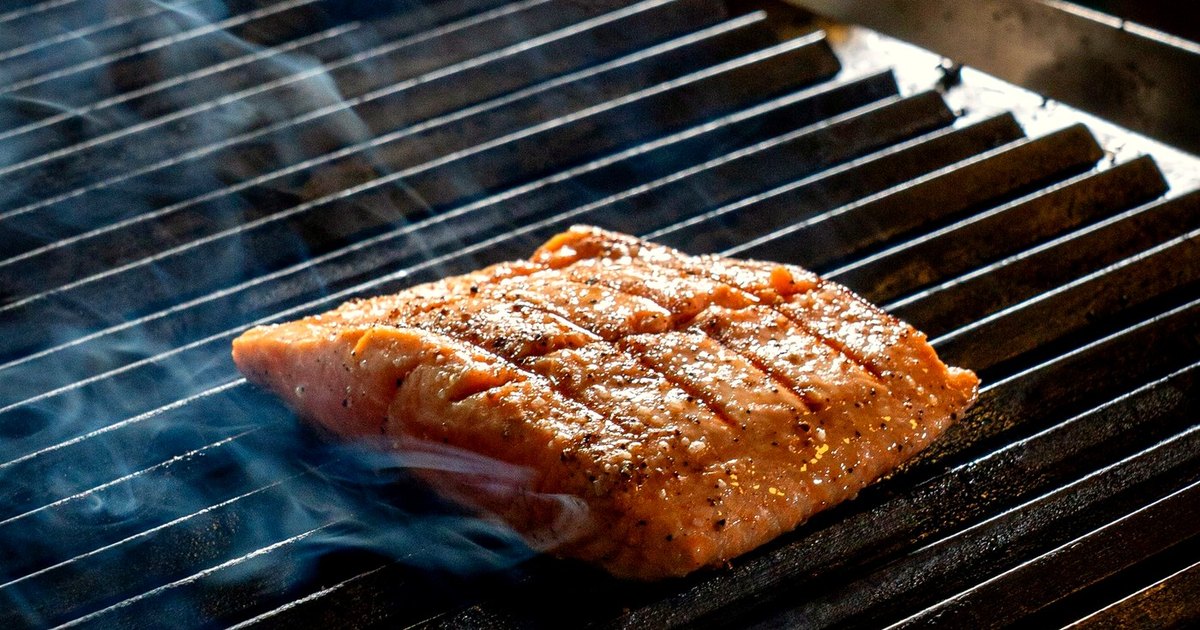 A seasoned fish fillet with grill marks on a hot grill